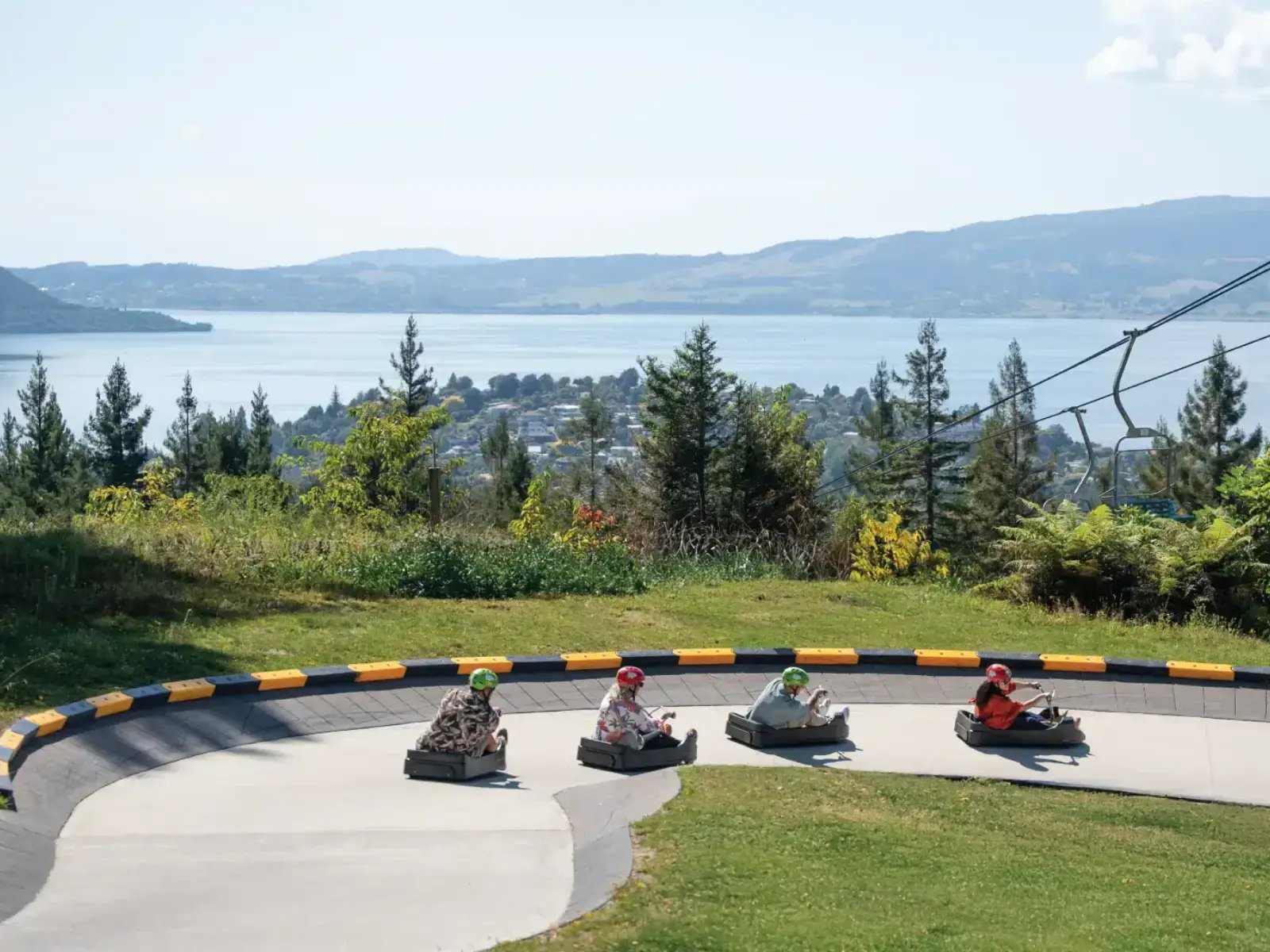 Group riding the Luge at Skyline Rotorua with sweeping views of Lake Rotorua and surrounding hills.
