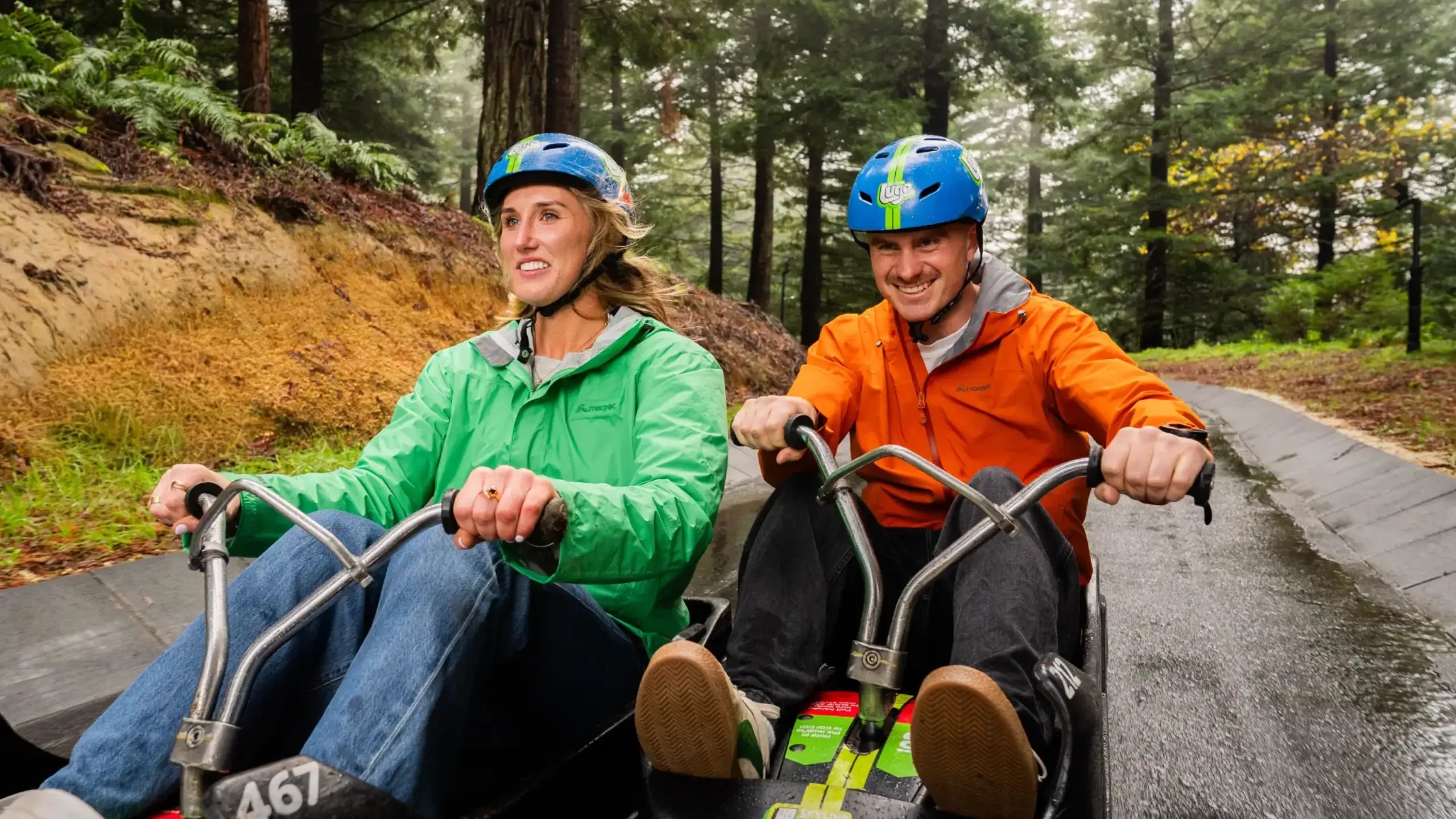 Two guests enjoying a Skyline Luge ride through the forest at Skyline Rotorua.