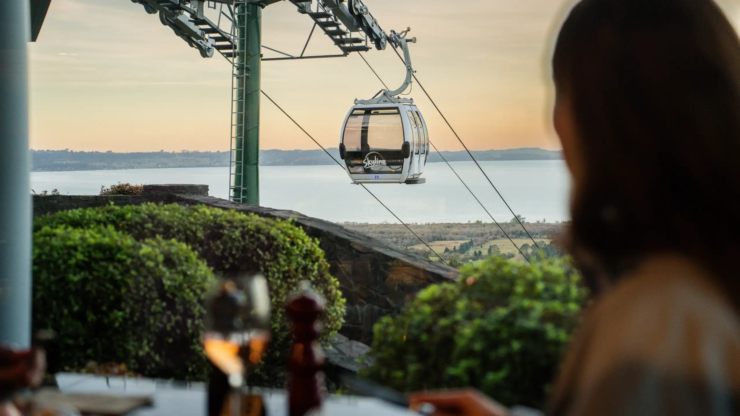 Skyline Gondola cabin travelling above Rotorua at sunset, viewed from Stratosfare Restaurant, with panoramic views across Lake Rotorua during the Graze by Stratosfare evening experience.