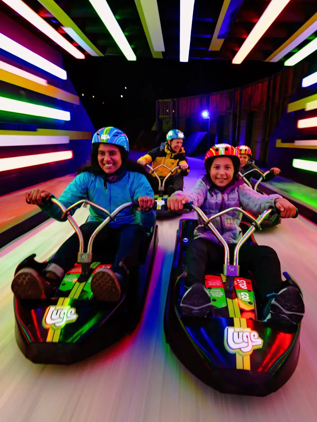 Family riding the Twilight Luge at Skyline Rotorua, zooming through a tunnel lit with colourful LED lights.