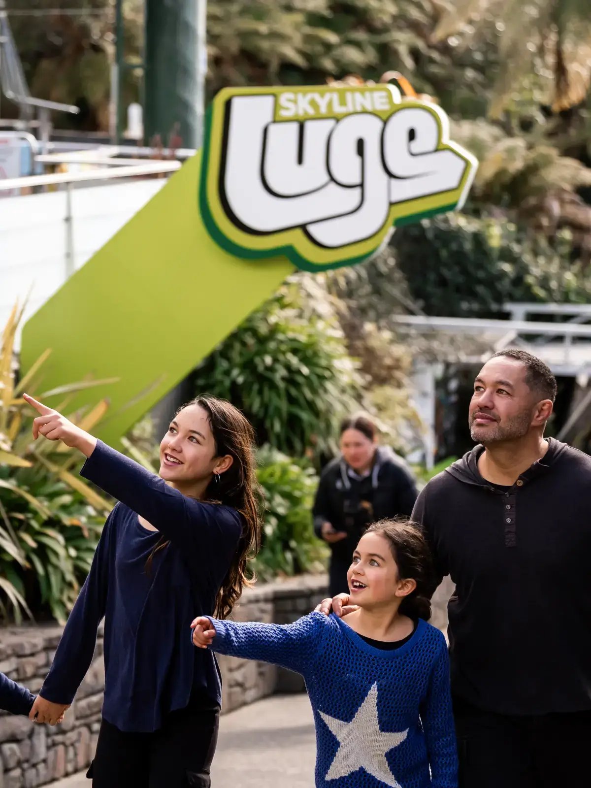 Family walking toward the Skyline Rotorua Luge entrance, smiling as a child excitedly points ahead.
