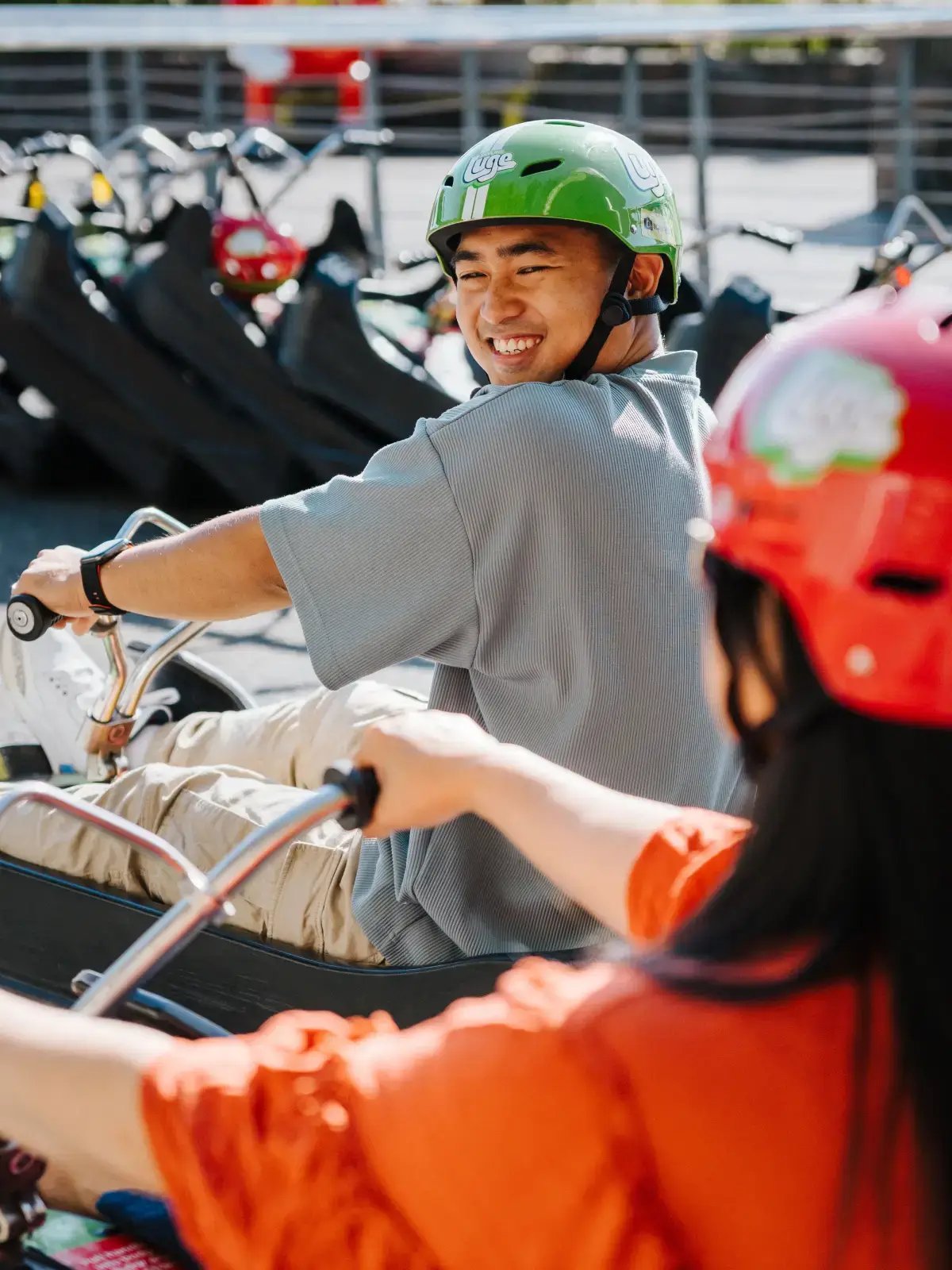 Two friends smiling as they get ready to ride the Luge at Skyline Rotorua, sitting in their carts near the track start.