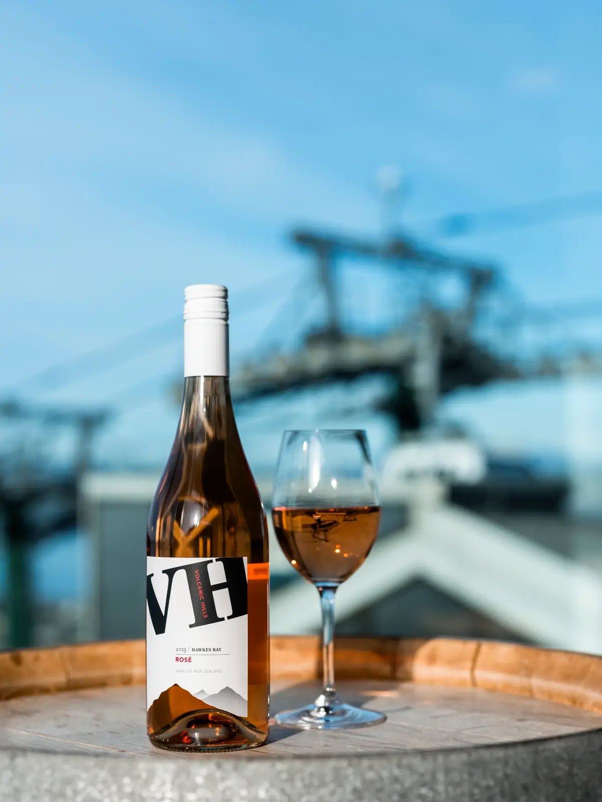 A bottle of Volcanic Hills Rosé and a glass of wine sit on a barrel with the Skyline Gondola blurred in the background.