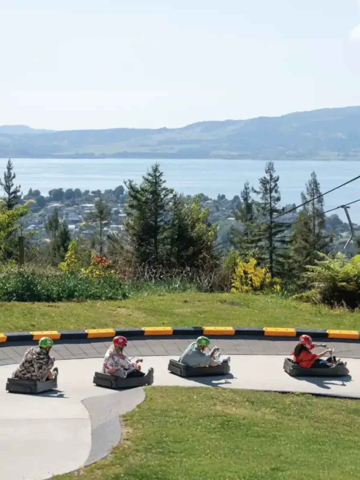 Guests riding the Luge at Skyline Rotorua with views over the lake