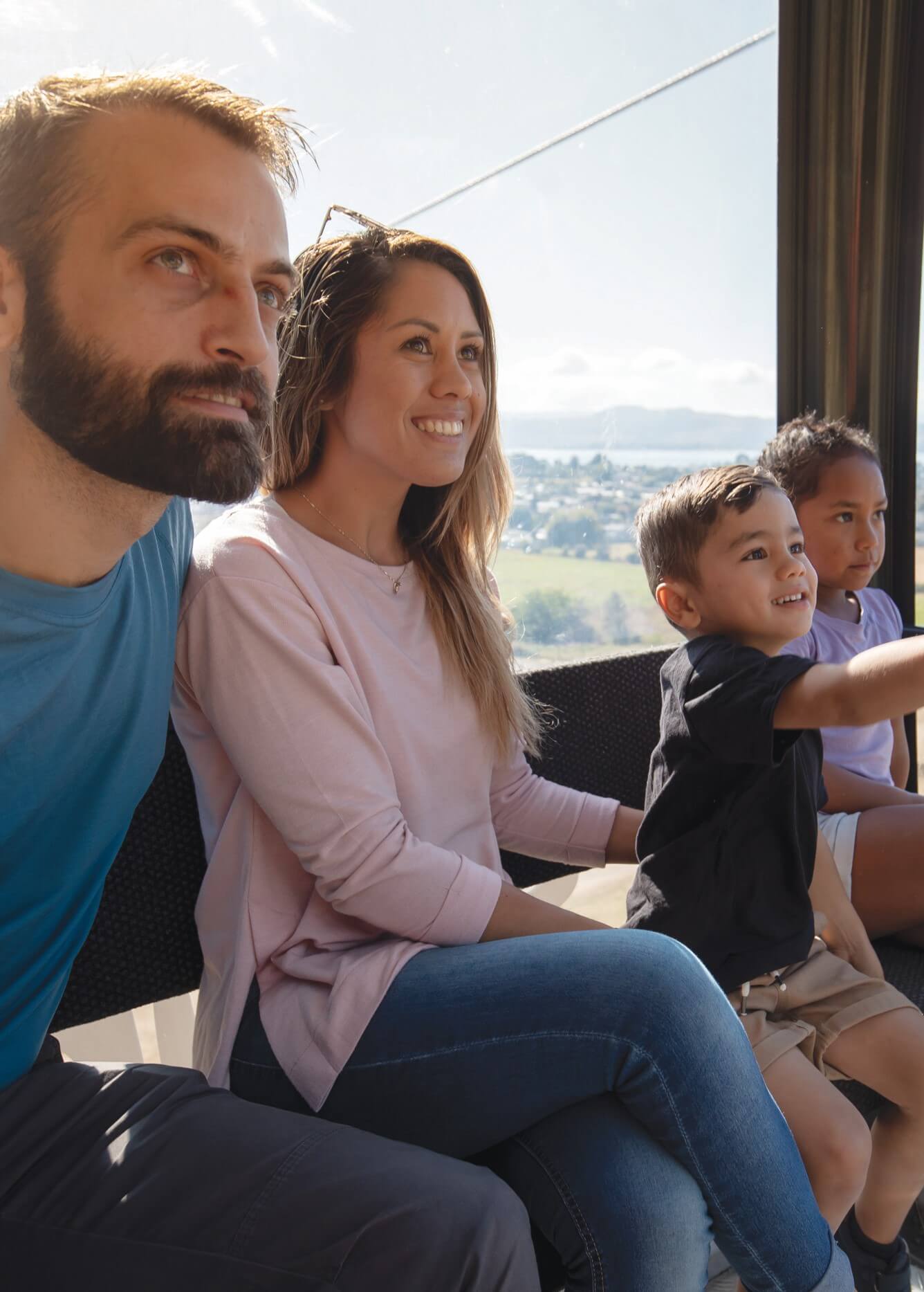 Family enjoying the Skyline Rotorua Gondola ride with views over the city and lake on a sunny day.