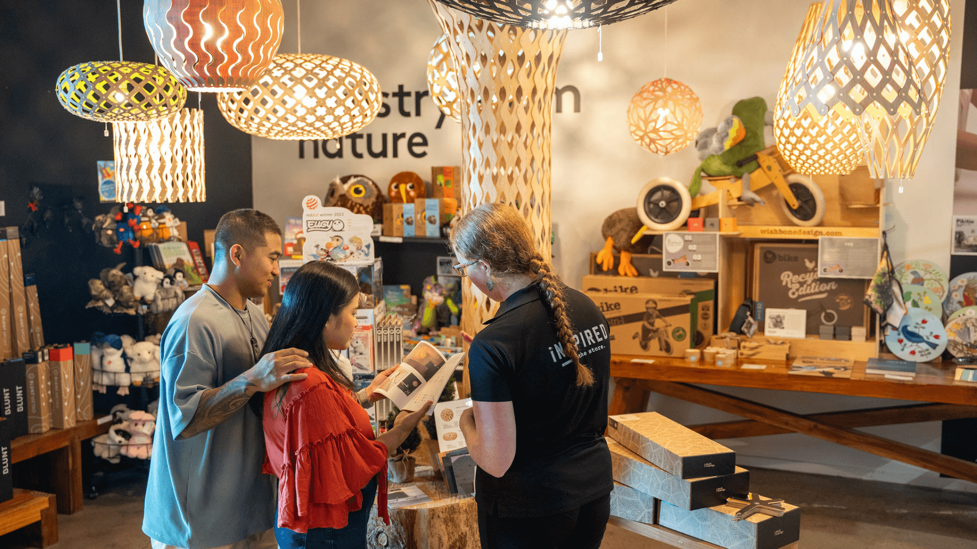 A Skyline Rotorua staff member shows a product catalogue to a couple under David Trubridge lights at the iNZpired store.