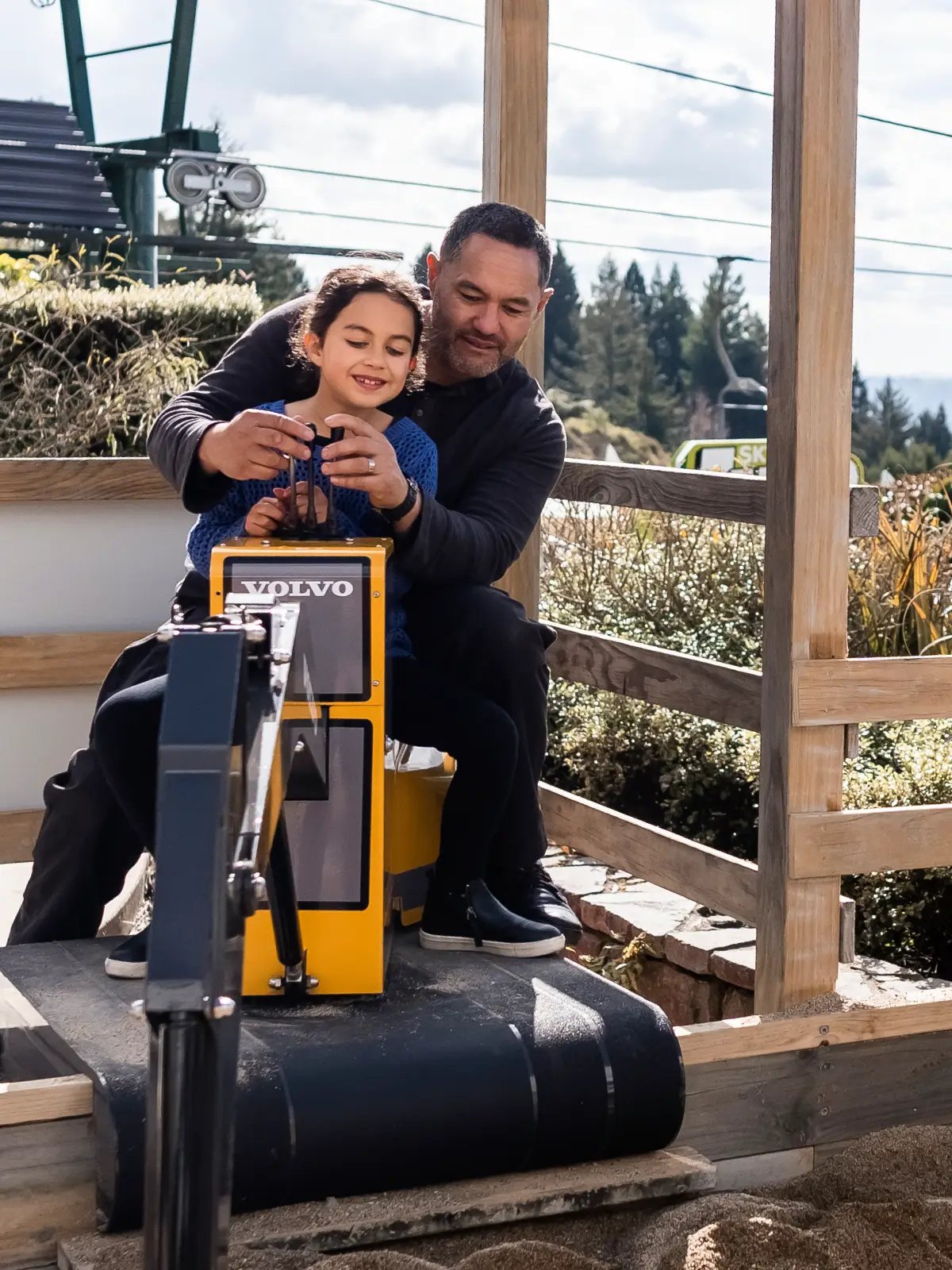 Father helping his child operate the Volvo digger attraction at Skyline Rotorua on a sunny day.