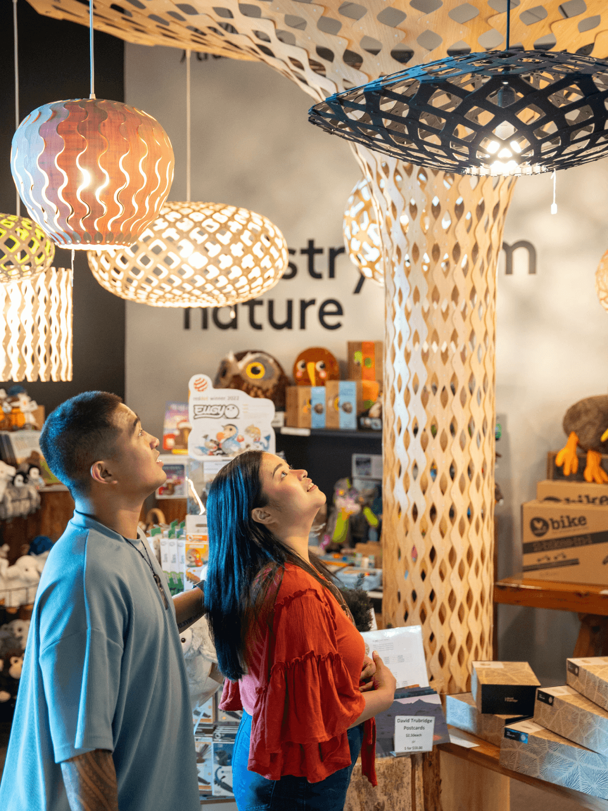 A couple admires David Trubridge pendant lights at the Skyline Rotorua iNZpired store, surrounded by gifts and wooden décor.
