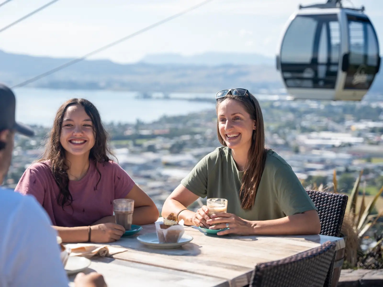 Friends enjoying coffee and muffins at Market Kitchen Café at Skyline Rotorua with gondola and lake views.