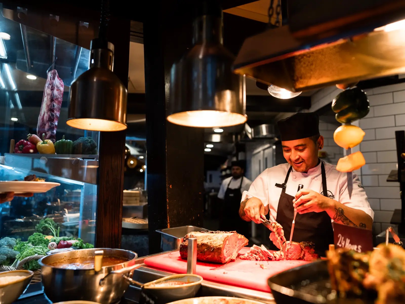 A Stratosfare chef smiles while carving a freshly roasted cut of meat under warm lights at the buffet station, surrounded by vegetables and serving dishes.