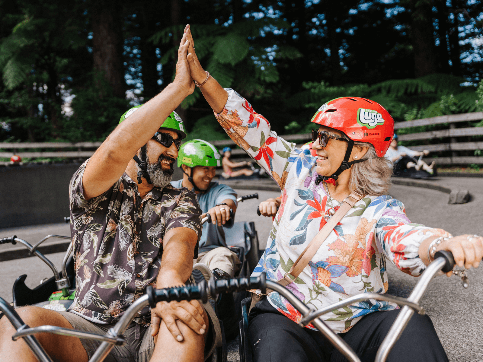 Two adults high-fiving after a fun Luge ride at Skyline Rotorua, celebrating together on the track surrounded by forest.